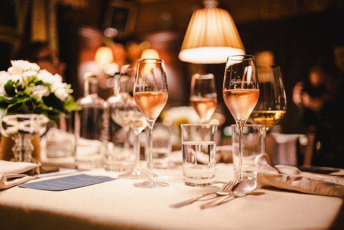 Ein festlich gedeckter Tisch mit verschiedenen Gläsern, einer Blumenvase und einem Hauch von Eleganz in der Beleuchtung.