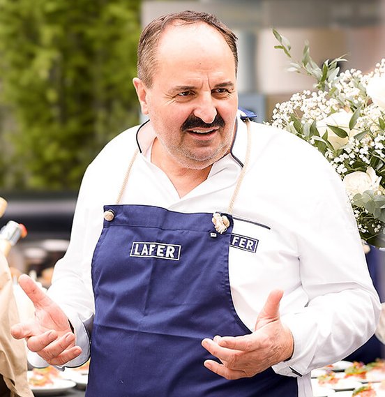 Ein lächelnder Mann in einem blauen Kochoutfit spricht leidenschaftlich, während eine Frau ihm aufmerksam zuhört.