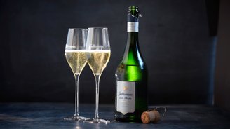 Zwei elegante Sektgläser mit sprudelndem Inhalt stehen neben einer Flasche Geldermann Sekt auf einem dunklen Tisch.