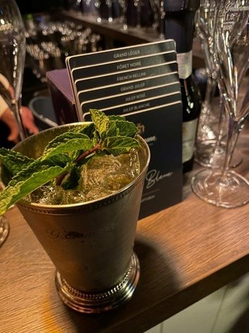 Ein eleganter Cocktail in einem silbernen Becher, garniert mit frischer Minze, steht auf einer Holztheke.