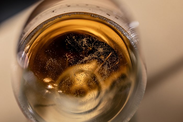 Ein Glas mit sprudelndem Getränk, das goldene Blasen aufweist, reflektiert sanftes Licht im Hintergrund.