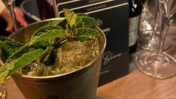 Ein eleganter Cocktail in einem silbernen Becher, garniert mit frischer Minze, steht auf einer Holztheke.