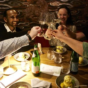 Eine Gruppe von Freunden hebt ihre Gläser in einem festlichen Toast, während sie an einem schön gedeckten Tisch sitzen.