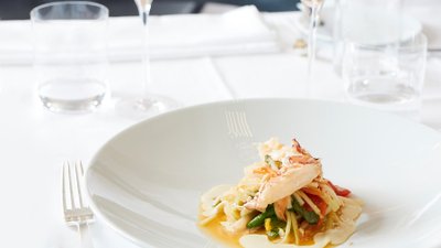 Ein Teller von Mario Lohningers Hummer mit Papayasalat und zwei Gläser Geldermann Grand Rosé auf einem schön gedeckten Tisch.