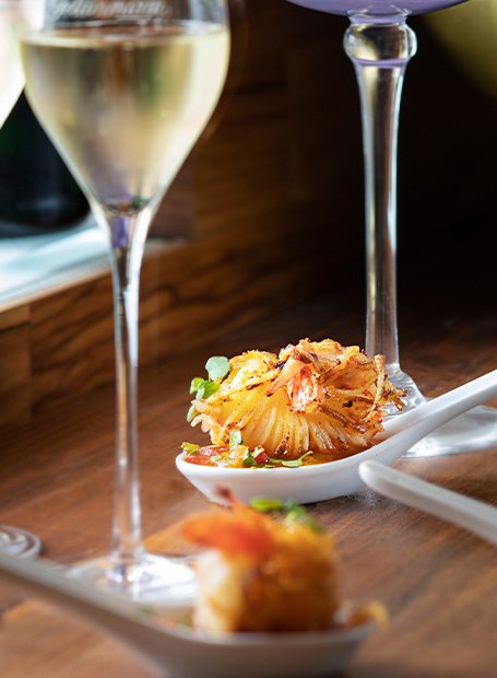 Auf einem Holzregal sind drei Sektgläser, eine Flasche Geldermann Grand Brut und appetitliche Garnelenhäppchen arrangiert.