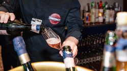 Ein Barkeeper schenkt sprudelnden Rosé in ein elegantes Glas, während Flaschen im Hintergrund sichtbar sind.