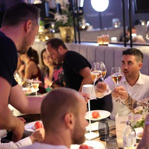 Eine Gruppe von Freunden hebt Gläser mit Roséwein an einem festlich gedeckten Tisch in einem eleganten Restaurant.