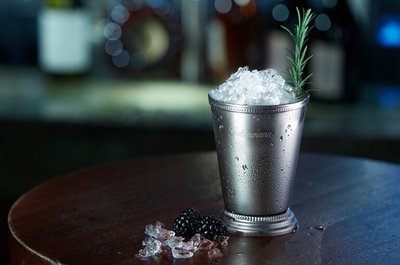 Silberner Becher gefüllt mit Crushed Ice und Thymian-Garnitur auf einem dunklen Holztisch.
