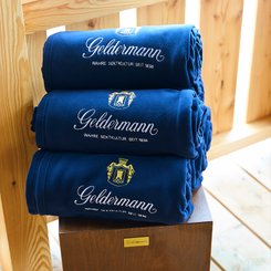 Geldermann Soirée Rosé: Ein Stapel dunkelblauer Fleece-Decken mit Geldermann-Logo