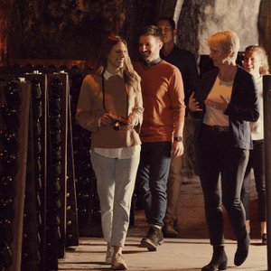 Die Gruppe von Freunden entdeckt die Weinsammlung im Keller, umgeben von Regalen voller Weinflaschen und warmem Licht.