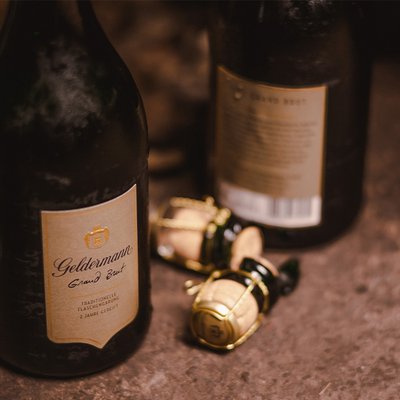 Zwei Flaschen Geldermann Sekt stehen auf einer rustikalen Oberfläche, umgeben von Korken und einem warmen, einladenden Licht.
