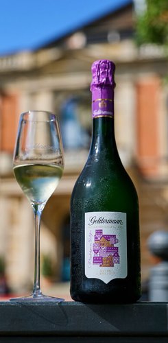 Eine Flasche und ein Glas mit der Bayreuther Festspiel Cuvée 2025 vor der Kulisse des Festpielhauses