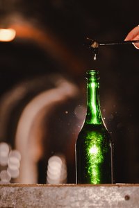 Eine grüne Flasche steht auf einem Tisch, während ein Tropfen von einem Löffel darüber fällt und die Umgebung leicht verschwommen ist.