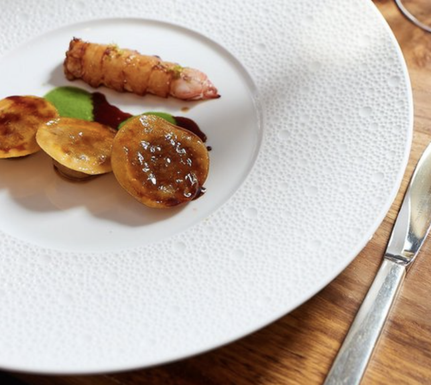 Ein stilvoll angerichtetes Gericht mit einer Garnele, goldbraunen Teigstücken und einer grünen Sauce auf einem eleganten Teller.