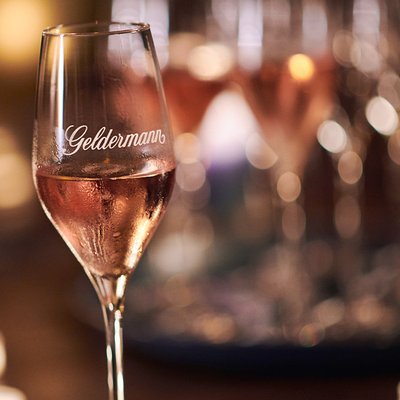 Das Glas mit der Aufschrift 'Geldermann' enthält sprudelnden rosé Sekt und wird von sanften Lichtern umgeben.