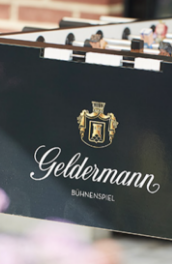 Ein Tischfußballspiel mit dem Logo 'Geldermann' und der Aufschrift 'BühnenSpiel' in einem sonnigen Außenbereich.