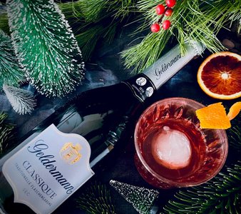 Der Cocktail mit Eis und einer Orangenscheibe wird von Tannenzweigen und einer Flasche Geldermann Sekt stilvoll ergänzt.