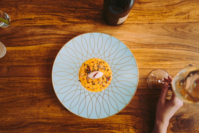 Auf einem blauen Teller liegt eine gelbe Speise, dekoriert mit essbaren Blüten und einer kleinen weißen Komponente in der Mitte.