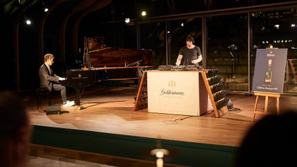 In einem stilvollen Veranstaltungsraum spielt ein Musiker am Klavier, während ein DJ im Hintergrund Beats mischt.