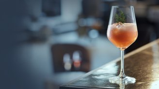 Auf einer polierten Theke steht ein Glas mit einem leuchtend orangefarbenen Getränk, das in einem modernen, gemütlichen Raum platziert ist.