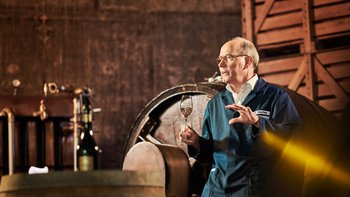 Älterer Mann in einem Weinkeller mit einem Glas Weißwein in der Hand