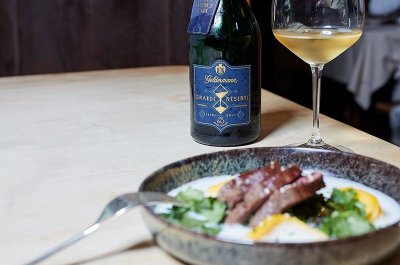 Ein Glas Weißwein steht neben einem Teller mit saftigem Fleisch, umgeben von buntem Gemüse und einer feinen Sauce.