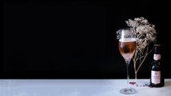 Ein elegantes Glas mit roséfarbenem Getränk steht auf einem Tisch, umgeben von zarten, trockenen Blumen und einer Flasche.