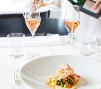 Zwei Gläser Roséwein stehen auf einem schön gedeckten Tisch, während ein Kellner Wein einschenkt und ein köstliches Gericht präsentiert.