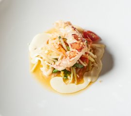 Ein kunstvoll angerichteter Teller mit einer Portion frischer Meeresfrüchte, Gemüse und einer cremigen Sauce in der Mitte.