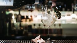 Ein Barkeeper gießt ein sprudelndes Getränk in ein Glas mit Eis, das mit einem kleinen Snack dekoriert ist.