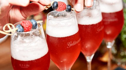 Ein festlicher Tisch mit drei Gläsern prickelndem Getränk, die mit frischen Beeren geschmückt sind, strahlt eine einladende Atmosphäre aus.