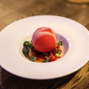 Ein elegantes Dessert mit einer roten, glänzenden Kugel, die auf einer fruchtigen Erdbeerbasis serviert wird.